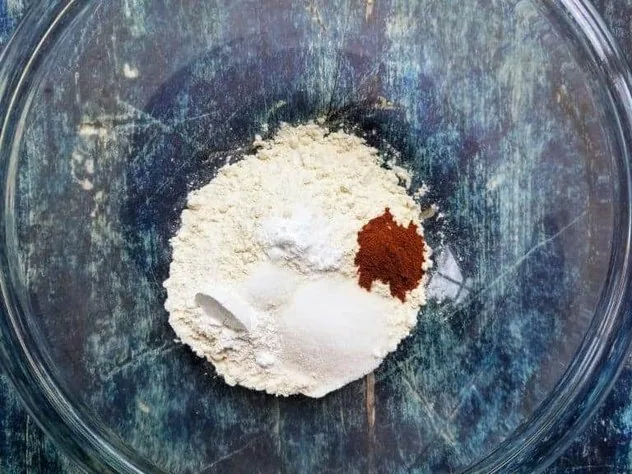 A pile of the dry ingredients in a large glass bowl on a blue background.