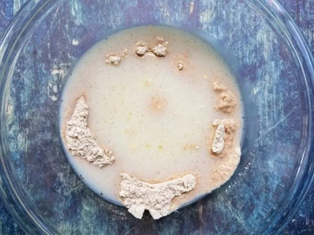 Liquid ingredients sitting in a well made by the dry ingredients in a large glass bowl on a blue background.