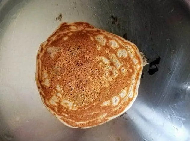 A fully cooked lightly golden colored blueberry buttermilk pancake in a stainless steel pan.