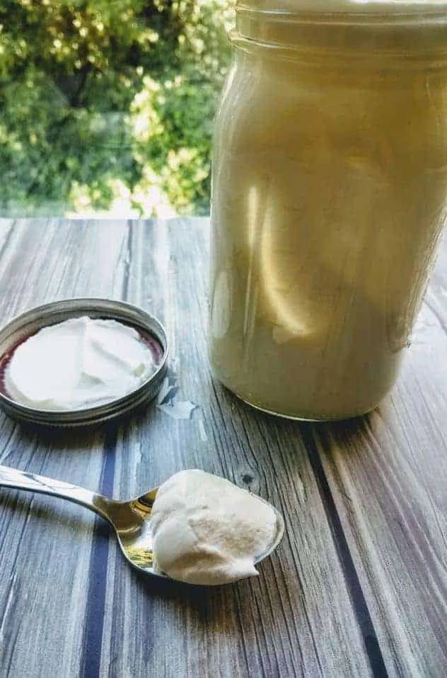 Homemade Butter Process Step 2a Whipped cream in a large mason jar on a gray wood plank background. A spoon with a scoop of whipped cream sits next to the jar.