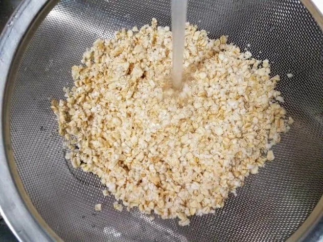 Homemade Oat Milk Process Step 2 Soaked oats being rinsed under running water in a fine mesh stainless steel sieve.