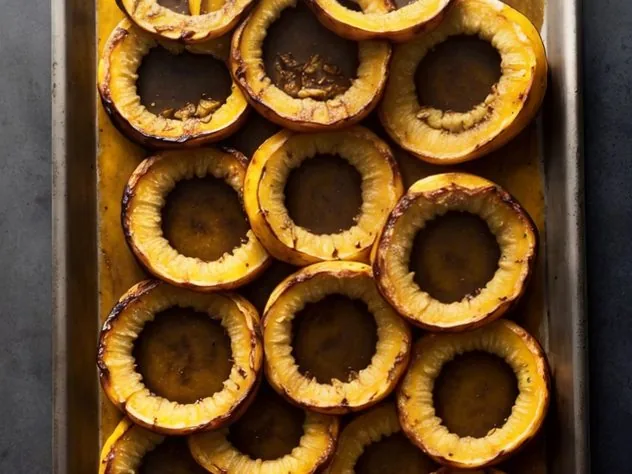 Roasted Delicata Squash Process Step 2b Half moon slices of delicata squash frame a small white bowl holding the scooped out seeds. Everything sits on a wooden cutting board.