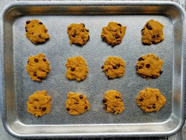Baked pumpkin chocolate chip cookies on a textured aluminum baking sheet.
