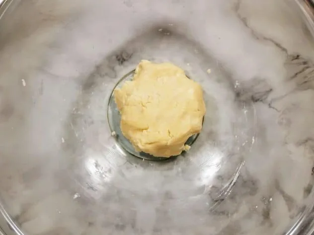 Chocolate Peanut Butter Balls Process Step 1 Confectioner's sugar, granulated sugar, butter, almond milk, and vanilla extract mixed together in a medium size glass bowl on a white marble background.