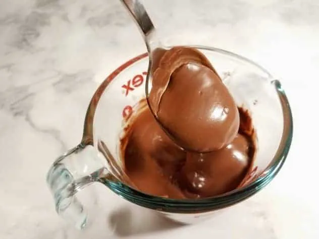 Chocolate Peanut Butter Balls Process Step 4 Melted chocolate chips and shortening in a glass Pyrex measuring cup. A spoon covered in the melted chocolate is being lifted out of the cup.
