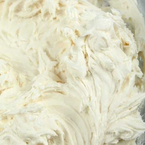 Vegan vanilla frosting sits in a large glass mixing bowl.