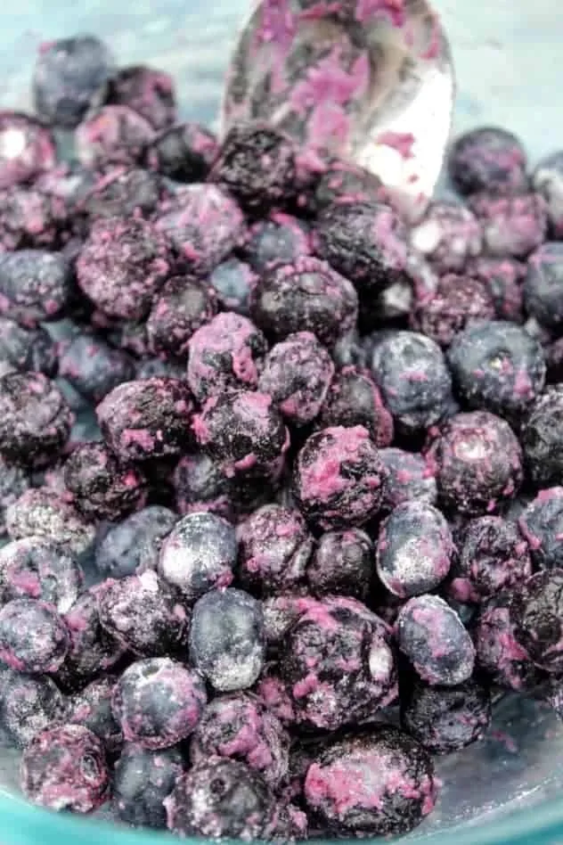 Blueberries coated with gluten-free flour sitting in a small glass bowl. A stainless steel mixing spoon sits at the top of the photo.