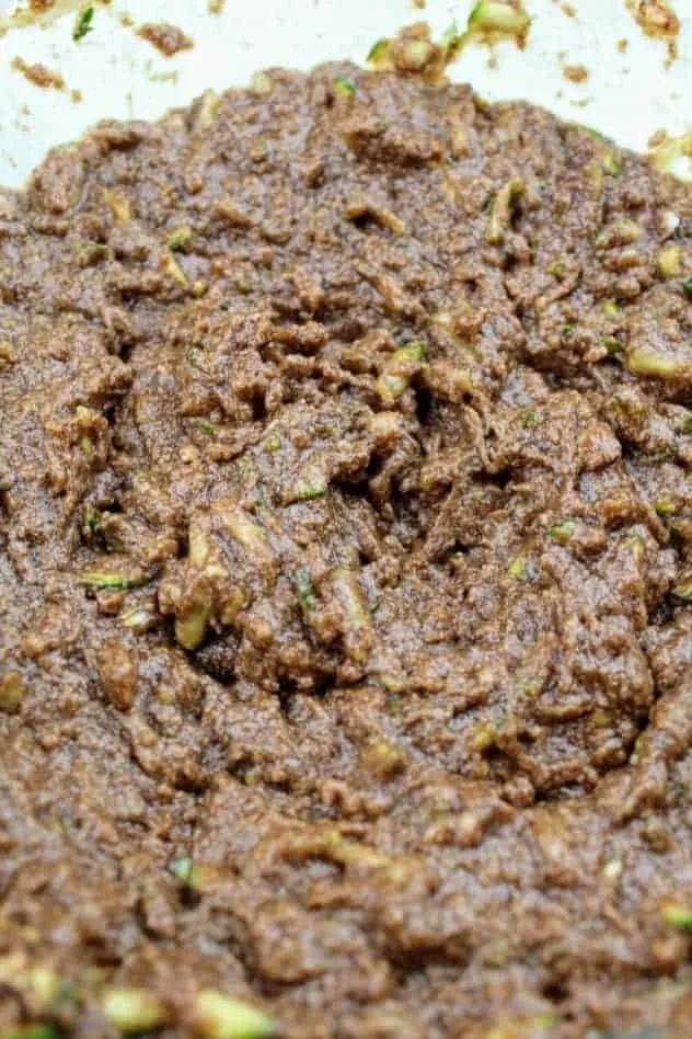 Vegan Chocolate Zucchini Cookies Process Step 1 A mixture of grated zucchini, light brown sugar, coconut oil, vegan butter, applesauce, vanilla extract, cinnamon, baking soda, cocoa powder, and Kosher salt in a large glass mixing bowl.