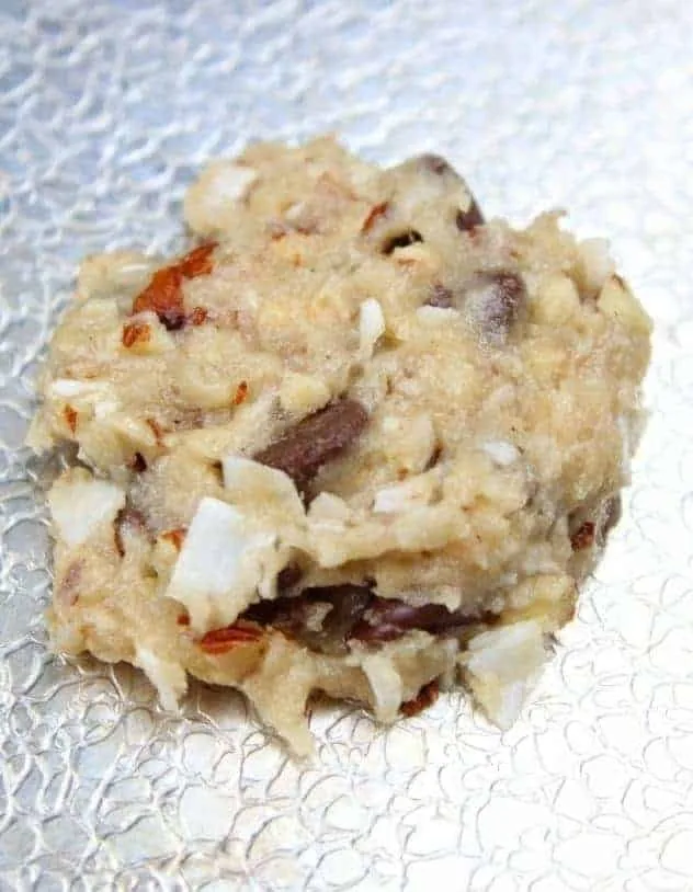 Vegan Almond Coconut Chocolate Chip Cookies Process Step 4 A single, flattened, unbaked vegan almond coconut chocolate chip cookie on a textured aluminum baking sheet.