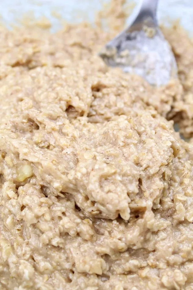 Vegan Banana Cookies Process Step 3 Addition of flour to the mixture to make a dough in a large glass mixing bowl with a stainless steel mixing spoon in the upper right.