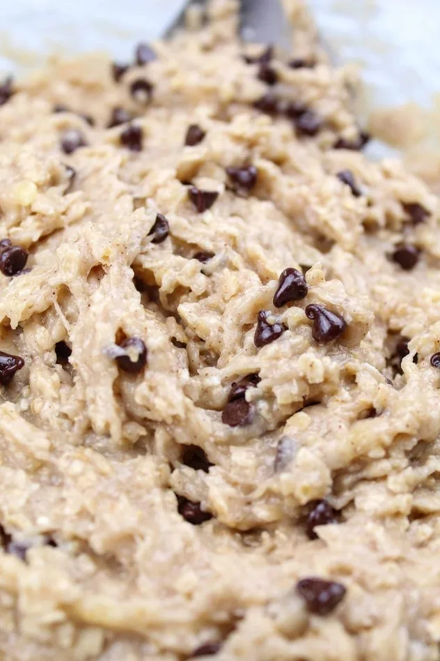 Vegan Banana Cookies Process Step 4 Addition of mini chocolate chips to the dough in a large glass mixing bowl with a stainless steel mixing spoon in the upper right.