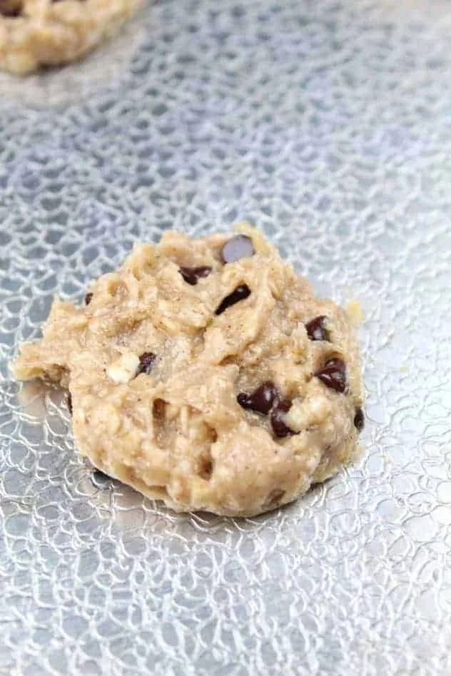 Vegan Banana Cookies Process Step 5 A single, flattened, unbaked cookie on a textured aluminum baking sheet.