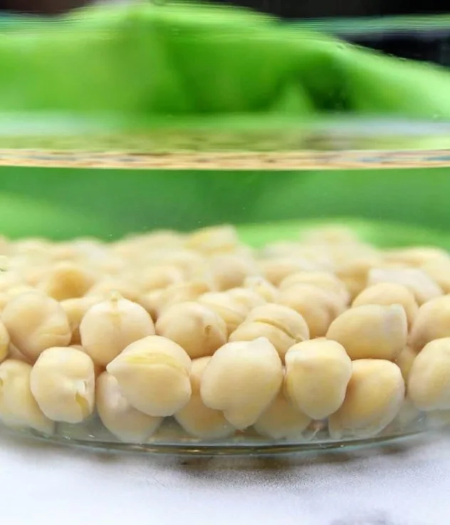 Vegan Key Lime Hummus Process Step 1 Chickpeas soak in a glass bowl filled with water. In the background is a lime green tea towel.