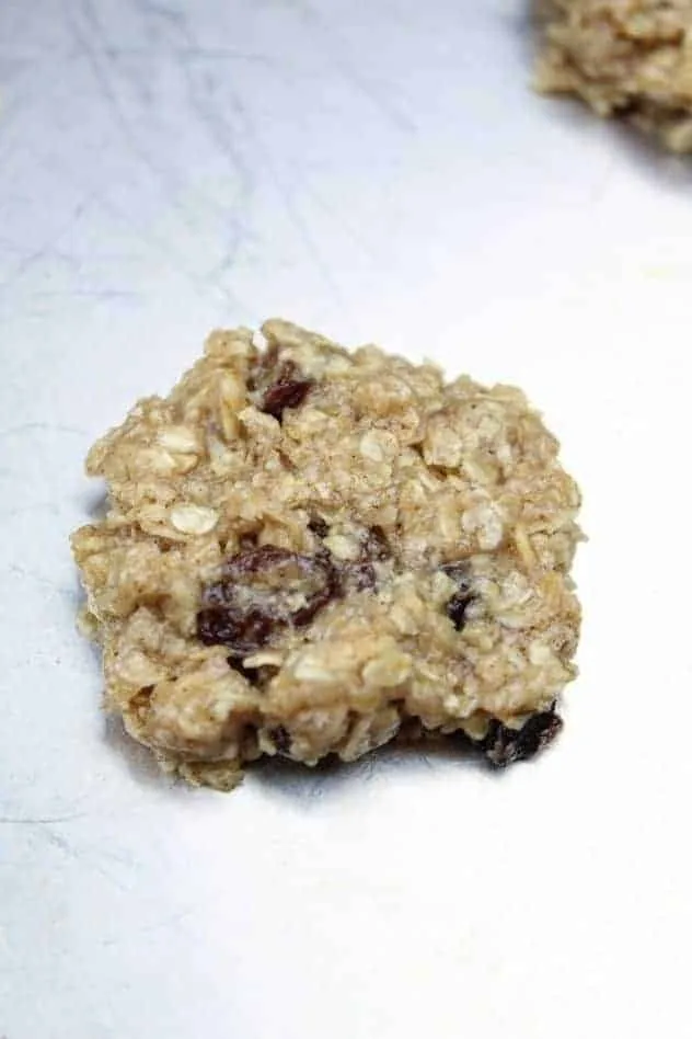 Vegan Oatmeal Raisin Cookies Process Step 4 A single vegan oatmeal raisin cookie sits on a greased aluminum baking sheet prior to baking.